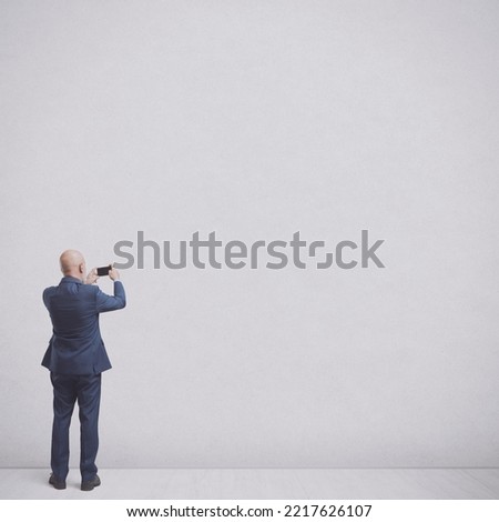 Businessman taking pictures of a blank wall in a room, back view