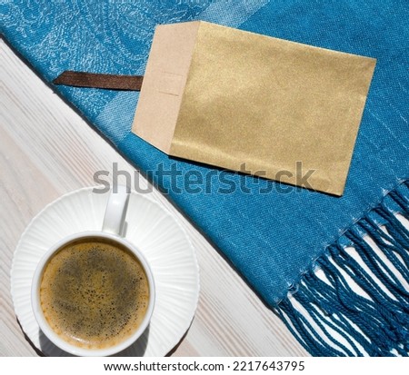 A cup of coffee, a saucer and a turquoise scarf on a white table. Romantic morning still life.
