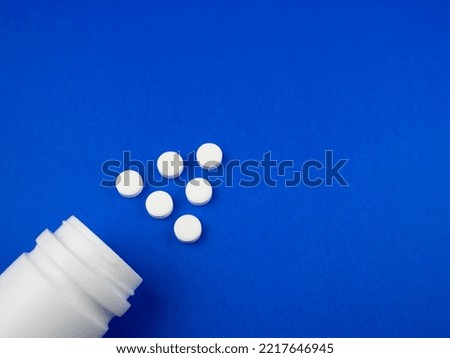 White pills from plastic medicine bottle on blue background