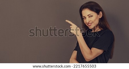 Beautiful positive business happy woman in black t-shirt showing the finger on empty copy space grey background. Closeup toned color