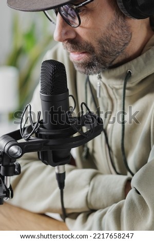 man records a podcast or audio content in a home office. a successful adult man with headphones and a microphone records text or music. online broadcast of an interview or recording of an audio