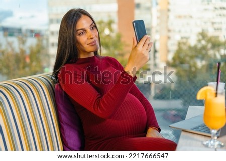 Shot of a young beautiful pregnant woman sitting in a restaurant taking a picture. Pregnant woman on a video call with a friend or a boyfriend