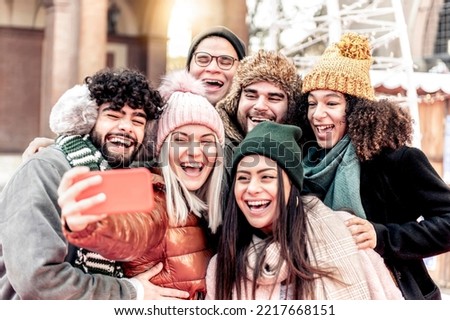 Multicultural happy friends having fun taking group selfie portrait on city street in a winter day - Multiracial young people celebrating laughing together outdoors - Happy lifestyle concept
