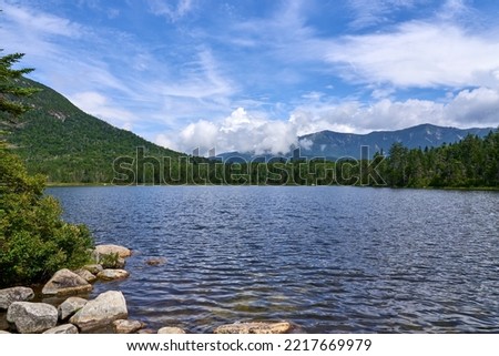 Lonesome Lake is a pristine glacial lake in Franconia Notch State Park in the White Mountains of NH, in Franconia, NH on a summer day with blue sky and dramatic clouds. Royalty-Free Stock Photo #2217669979