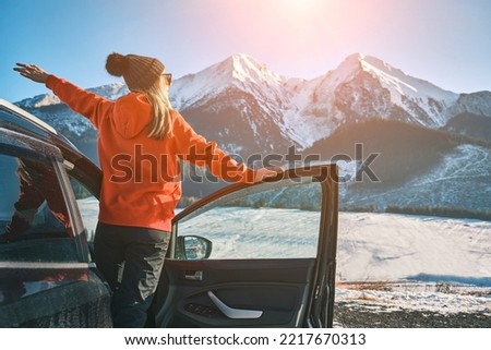 Woman traveling exploring, enjoying the view of the mountains, landscape, lifestyle concept winter vacation outdoors. Female standing near the car in sunny day, travel in the mountains, freedom.