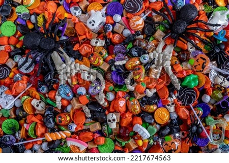 Scary Halloween skeleton hands filled with candy coming up out of a variety of Halloween candy spread out on table top and 2 big black glitter spiders