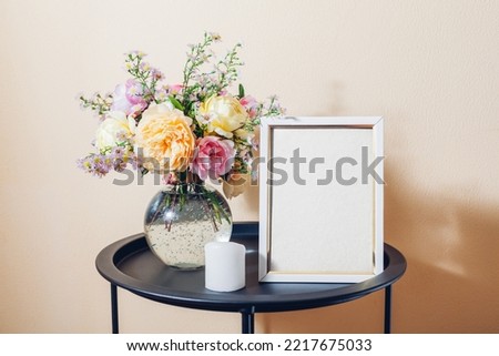 Empty blank mock-up of white photo frame with bouquet of roses and candle. Home interior decor on table. Space on white background