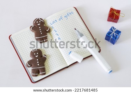 Notepad with gift list template, gingerbread men and gift boxes on white. Concept of congratulations on the new year and Christmas and making a list of gifts. Copy space. Daylight