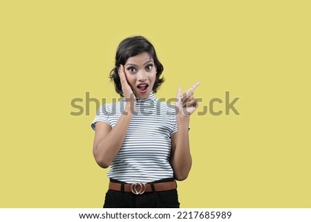 amazed shocked woman pointing finger on side looking into camera standing over yellow background.