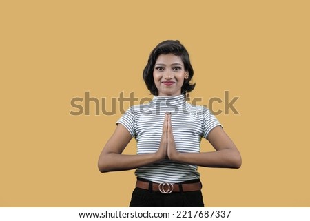 of Beautiful happy smiling Woman looking into camera, joining hands, Doing Namaste Greeting gesture, Isolated On orange Background