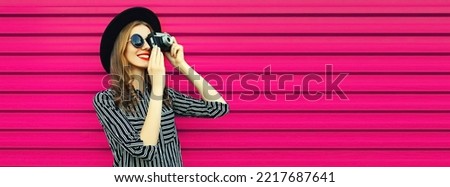Portrait of happy smiling young woman photographer with film camera on pink background