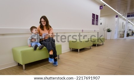 Mother and baby with a mobile phone in the clinic waiting for a pediatrician. Parent with a child boy with a smartphone in his hands. Kid is a boy aged one year and three months