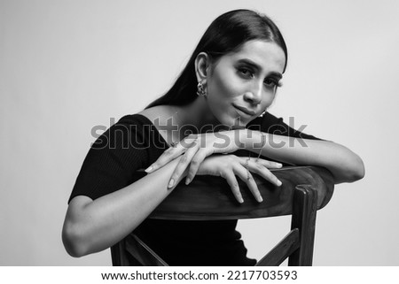 Stunning black and white portrait of a gorgeous woman leisurely seated on a wooden chair. Royalty-Free Stock Photo #2217703593