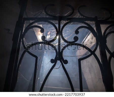 Horror Halloween concept. Creepy abandoned castle. An old candlestick and Halloween pumpkin glowing on wooden stairs with lattice door at night. Decoration with backlight and fog. Selective focus