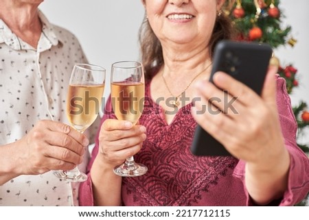 Unrecognizable adult hispanic couple talking by video call with a smartphone while toasting during Christmas or New Year, celebrating holidays at home, together.