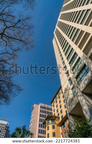 View of mid rise buildings from below at River Walk in San Antonio, Texas. Low angle view of buildings with trees against the blue sky.