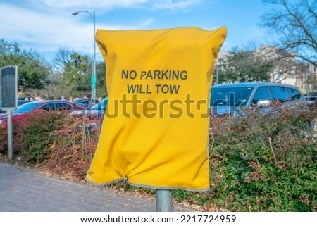 No Parking Will Tow sign on sidewalk in front of a parking lot in Austin Texas. Close up view of a bright yellow cloth signage with printed text informing drivers that parking is not allowed.
