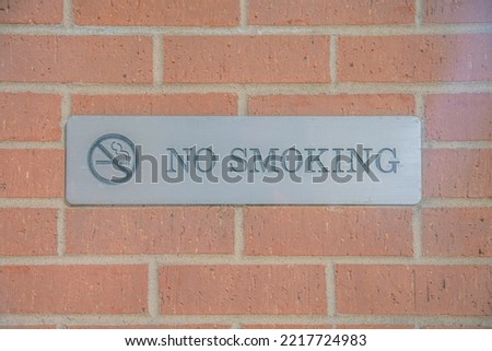 No Smoking sign debossed on a metal plate against brick wall of a building. Outdoor views in Austin Texas with close up of a signage prohibiting use of cigarette in the area.