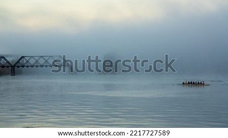 Rowing team in the fog. High quality photo of a foggy river with bridges in the background. With faces of the team naturally blurred by shutter speed.