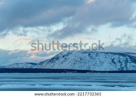 Stunning frozen lake in winter with snow capped mountains background. 