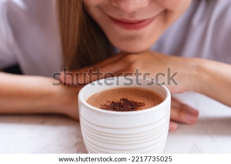 Closeup image of a beautiful woman looking and smelling a cup of hot chocolate