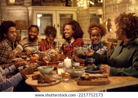 Happy African American family enjoying in lunch while celebrating Thanksgiving at dining table. Focus is on girl passing food to her grandmother.
