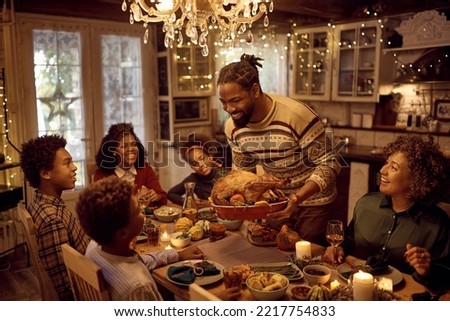 Mature black father serving traditional Thanksgiving turkey during family meal at dining table.