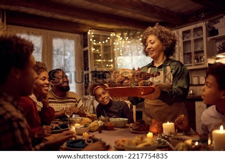 Happy mature African American woman serving stuffed turkey while having dinner with her extended family in dining room.