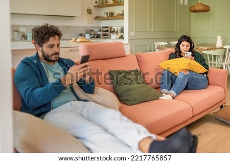 Young married couple using smart phone ignoring each other addicted to the internet and social network - man and woman phubbing in the living room - family people loneliness and technology lifestyle