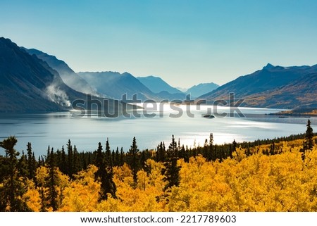 Windy Arm of Tagish Lake near Carcross, Yukon Territory YT, Canada, in autumn fall colors with wildfire still smoldering in forest of distant lake shore and mountain slope Royalty-Free Stock Photo #2217789603
