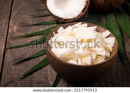 Coconut chips with coconut and green leaves on wooden background.  Royalty-Free Stock Photo #2217795913