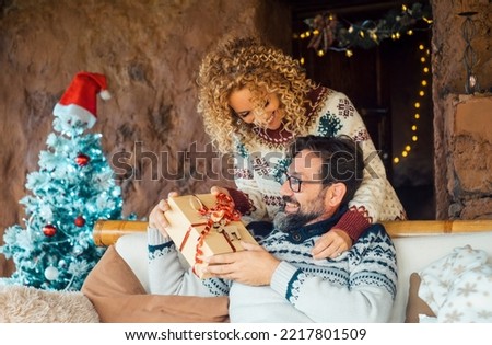 Christmas gifts exchange tradition concept. Happy couple enjoy xmas time holiday at home sharing presents. Woman doing a surprise to her husband man giving him a christmas gift from back. Joy people Royalty-Free Stock Photo #2217801509