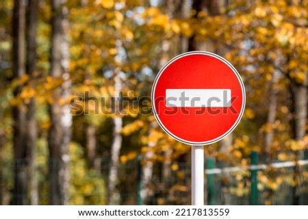 Red road sign "Entry prohibited" on the background of yellow autumn leaves. The road is closed with a red round sign. White brick in the red circle of the road sign.