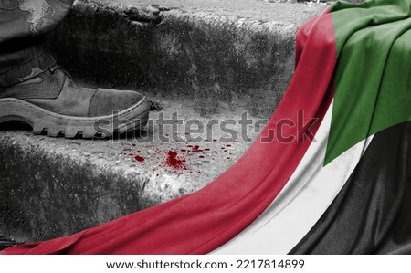 The leg of the military stands on the step next to the flag of Sudan, the concept of military conflict Royalty-Free Stock Photo #2217814899