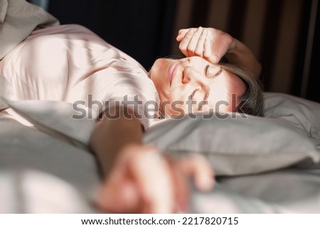 Beautiful middle aged woman waking up in her bed in the bedroom, happy 40s female is stretching and smiling Royalty-Free Stock Photo #2217820715