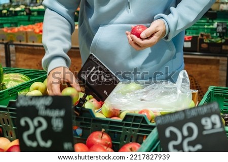 A man buys food, . A male customer chooses apples, taking products from the shelves in the store
