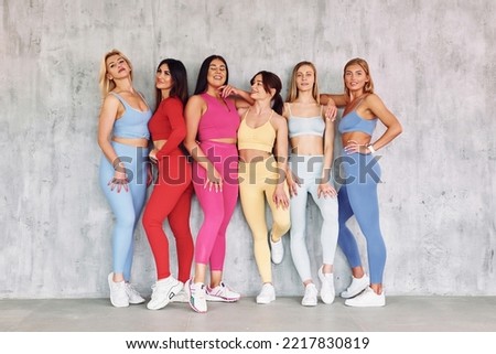 Group of positive people is posing for the camera. Beautiful women in sportive clothes is indoors in the studio.