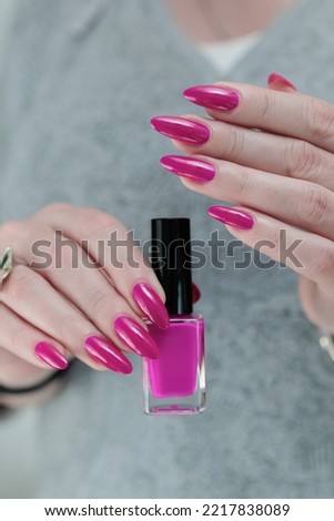 Female hand with long nails and a bottle bright neon pink fuchsia color nail polish
