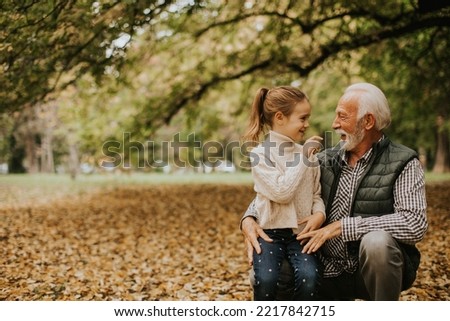 Handsome grandfather spending time with his granddaughter in park on autumn day Royalty-Free Stock Photo #2217842715