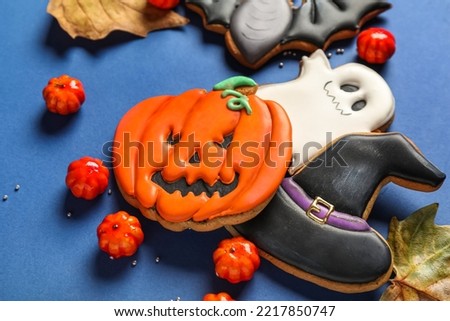 Tasty Halloween cookies, candies and fallen leaves on blue background, closeup