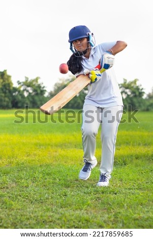 Female Indian cricket player wearing protective gear and hitting the ball with a bat on the field Royalty-Free Stock Photo #2217859685