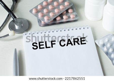 Self Care text text on a notebook on a table next to medicine, stethoscope, medical concept