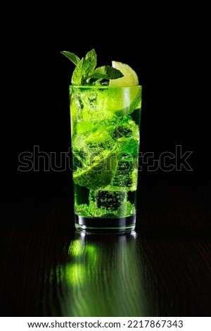 Green tarragon lemonade with lime slices and mint in a tall glass on a black background.