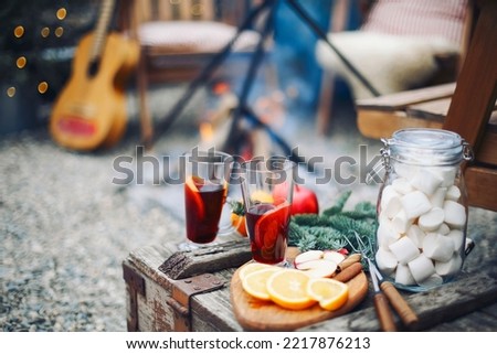 Two glasses of hot mulled wine drink with citrus, apples, cinnamon sticks, cloves and anise on wooden table background. Outdoors
