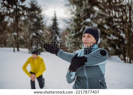 Senior couple warming-up and stretching in snowy forest before winter hike.