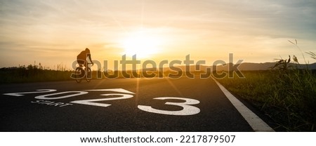 New year 2023 or start straight and beginning concept.silhouette of Blurry Man ride on bike and word 2023 start written on the road at sunset.Concept of challenge or career path,business strategy. Royalty-Free Stock Photo #2217879507