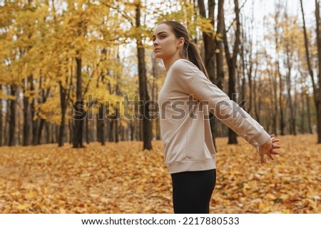 Side view of athletic woman in sportswear
stretching arms behind back while training in park in fall season 