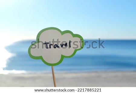 Stick with paper speech bubble with words Travel on background blue sea, sky, sandy beach on sunny summer day. Text-balloons with text from letters. Concept, symbol, sign vacation travel tourism rest