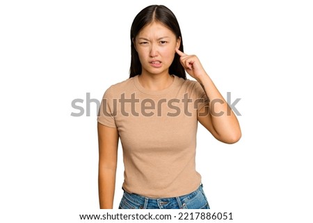 Young Asian woman isolated on green chroma background covering ears with fingers, stressed and desperate by a loudly ambient.