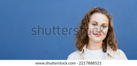 Portrait of smiling happy caucasian curly girl, student looking at camera over blue background. Real people. Banner with copy space.
